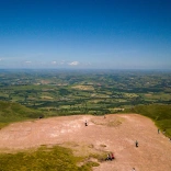 Aerial view of the green plains below from the top of Pen y Fan with blue skies.
